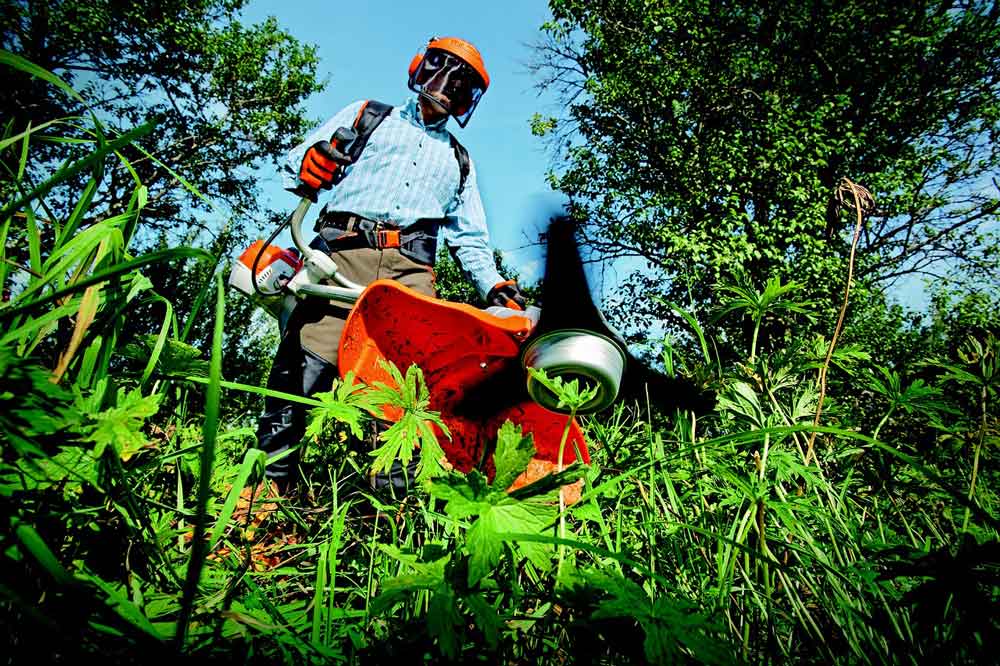 Crew member brush-cutting overgrowth in safety gear
